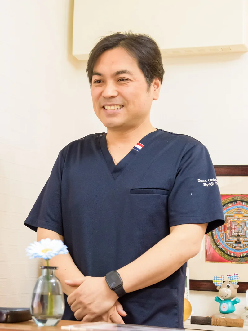 受付のカウンター越しに、お客様へ笑顔で話しかける Tono Osteopathy 院長 塔野亮二
