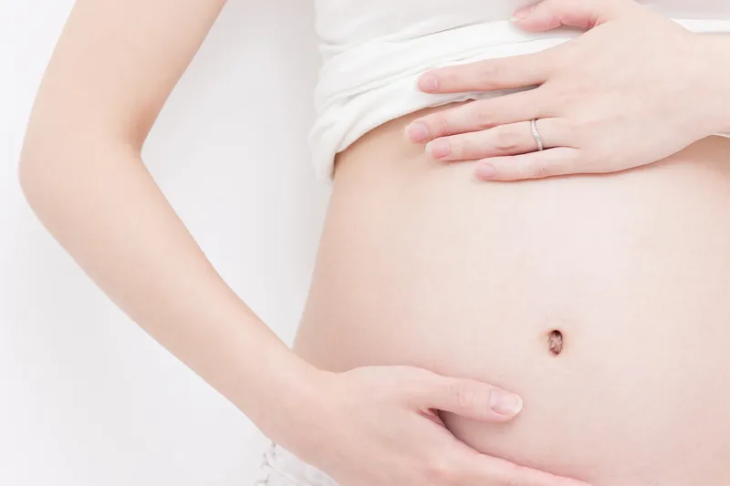 妊娠中の女性のお腹に、両手をそっと添えているところ