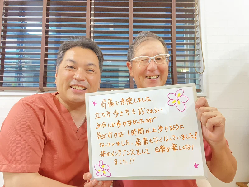 「肩痛で来院しました。立ち方、歩き方も診てもらい、30分しか歩けなかったのが気が付けば1時間以上歩けるようになっていました。肩痛もなくなっていました。体のメンテナンスをして、日常が楽しくなりました!!」と書かれたボードを、男性のお客様と院長が一緒に持っているところ