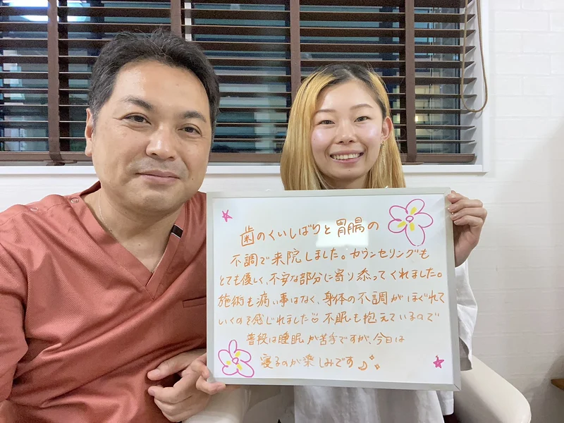「歯のくいしばりと胃腸の不調で来院しました。カウンセリングもとても優しく、不安な部分に寄り添ってくれました。施術も痛い事はなく、身体の不調がほぐれていくのを感じれました。不眠も抱えているので普段は睡眠が苦手ですが、今日は寝るのが楽しみです」と書かれたボードを、女性のお客様と院長が一緒に持っているところ